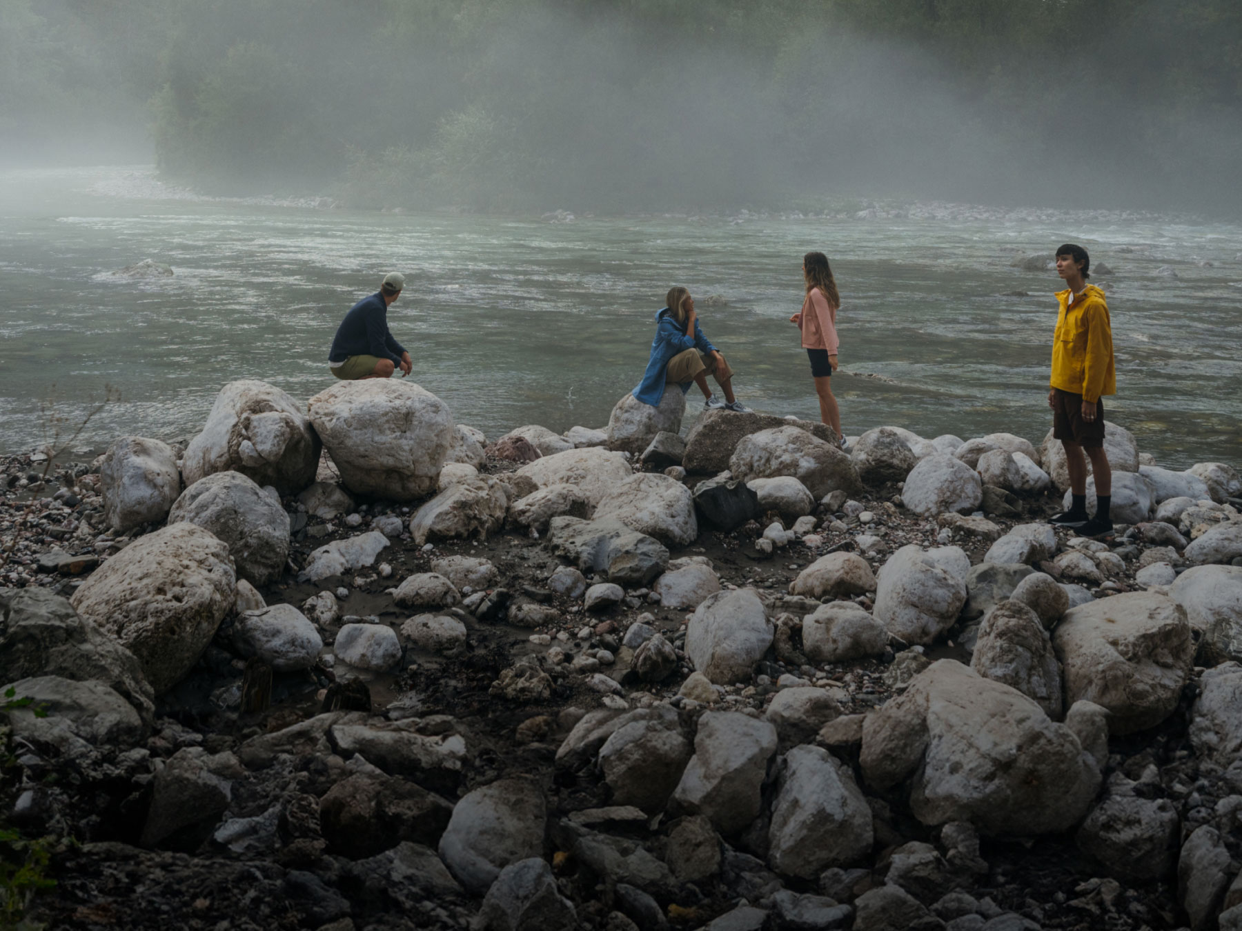 Foggy landscape and river with 4 people on rocks in the foreground